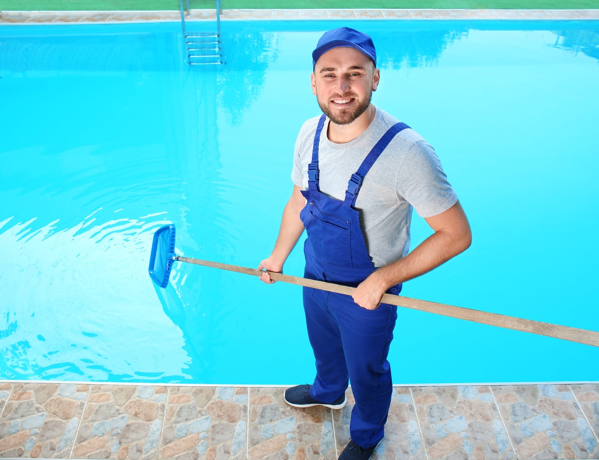 Pool contractor in blue overalls cleaning a residential pool, representing AdeptPlus web marketing services for pool companies